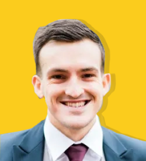 Rob Klarner headshot. Yellow background. Caucasian man with short but thick brown hair. He is wearing a white shirt, red tie, and black blazer.